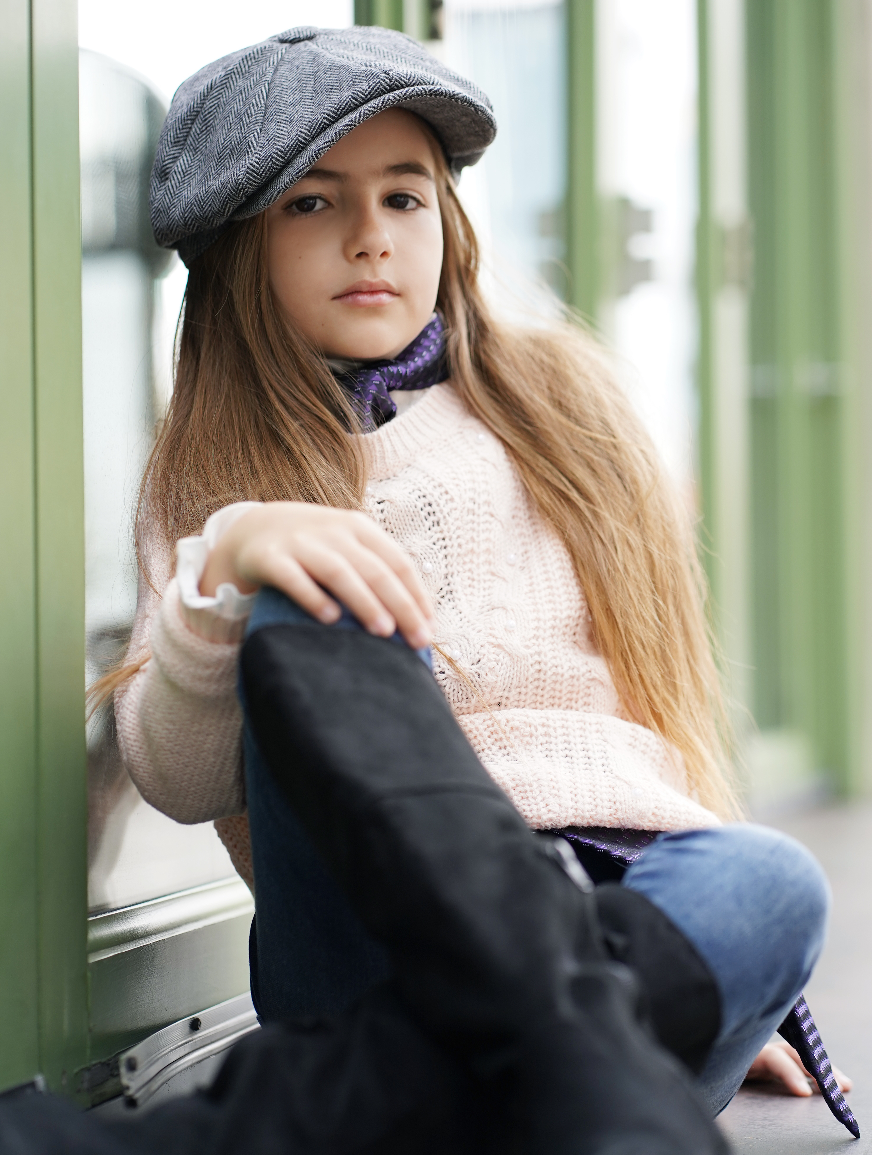 Natural-light portrait wearing a newsboy cap beside a green window frame
